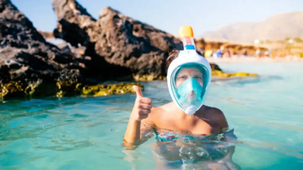 A girl wearing a full-face snorkel mask is standing in the water