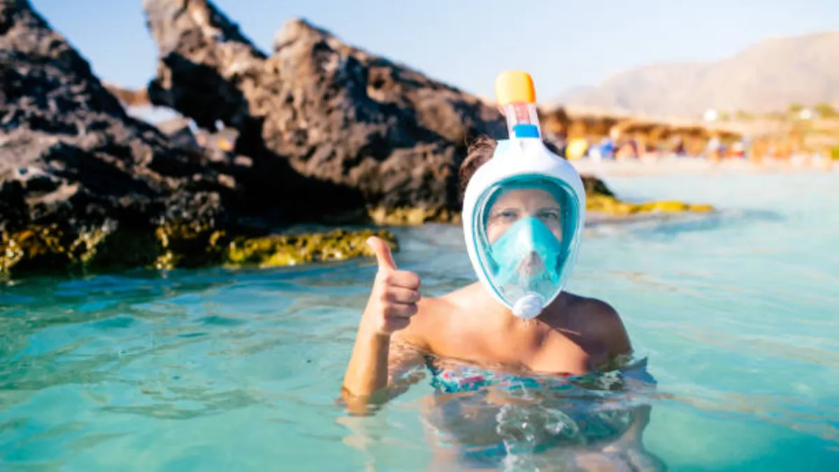 A girl wearing a full-face snorkel mask is standing in the water