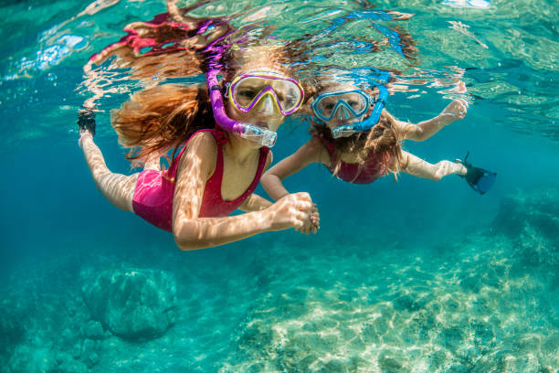 Two girls in pink swimsuits enjoy playing underwater and snorkeling in the crystal clear water